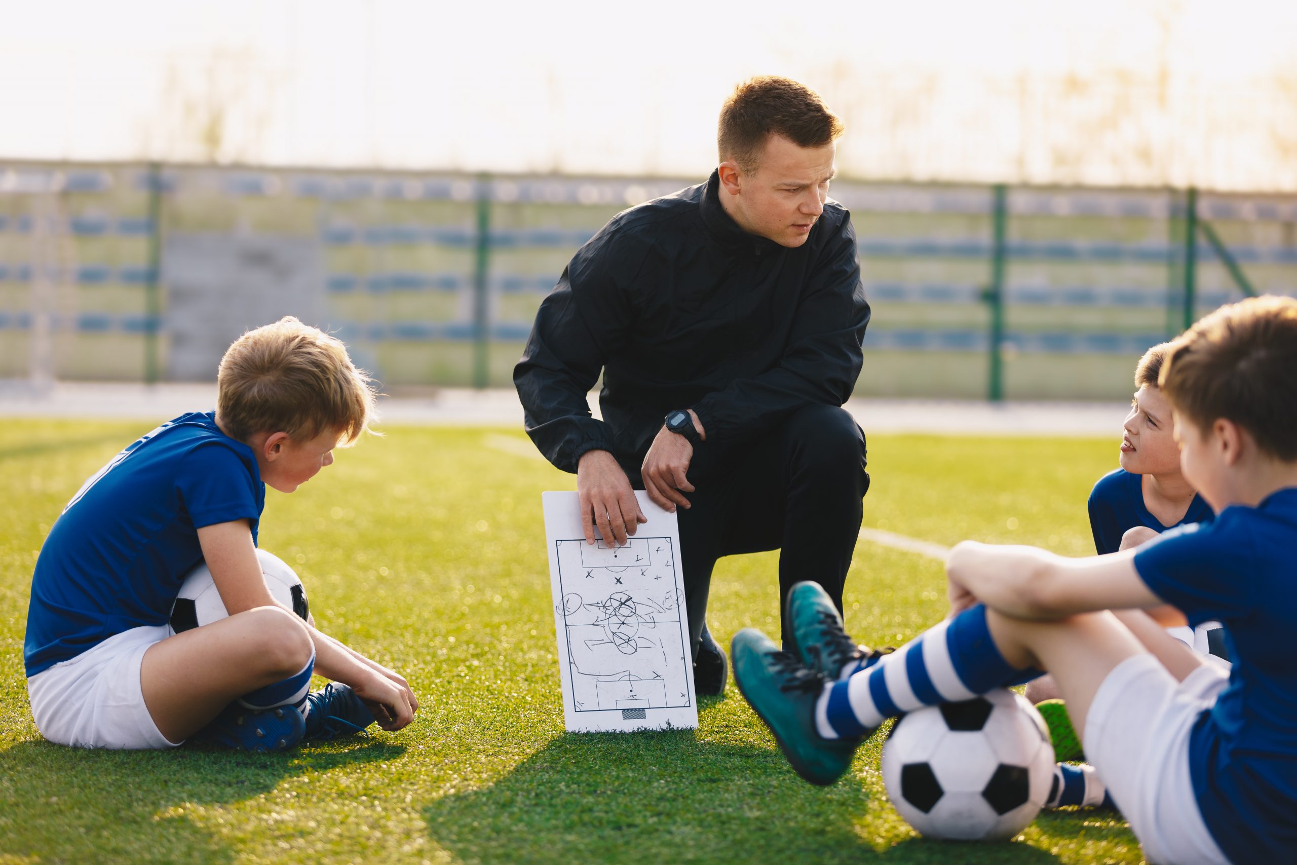 Football coach coaching children. Soccer football training session for children. Young coach teaching kids on football field. Football tactic education. Coach explains the strategy of the game