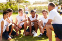 Huddle of five young male soccer athletes with coach.