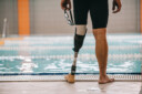 cropped shot of swimmer with artificial leg standing in front of indoor swimming pool and holding swimming goggles