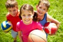 Three smiling kids with an assortment of sports equipment