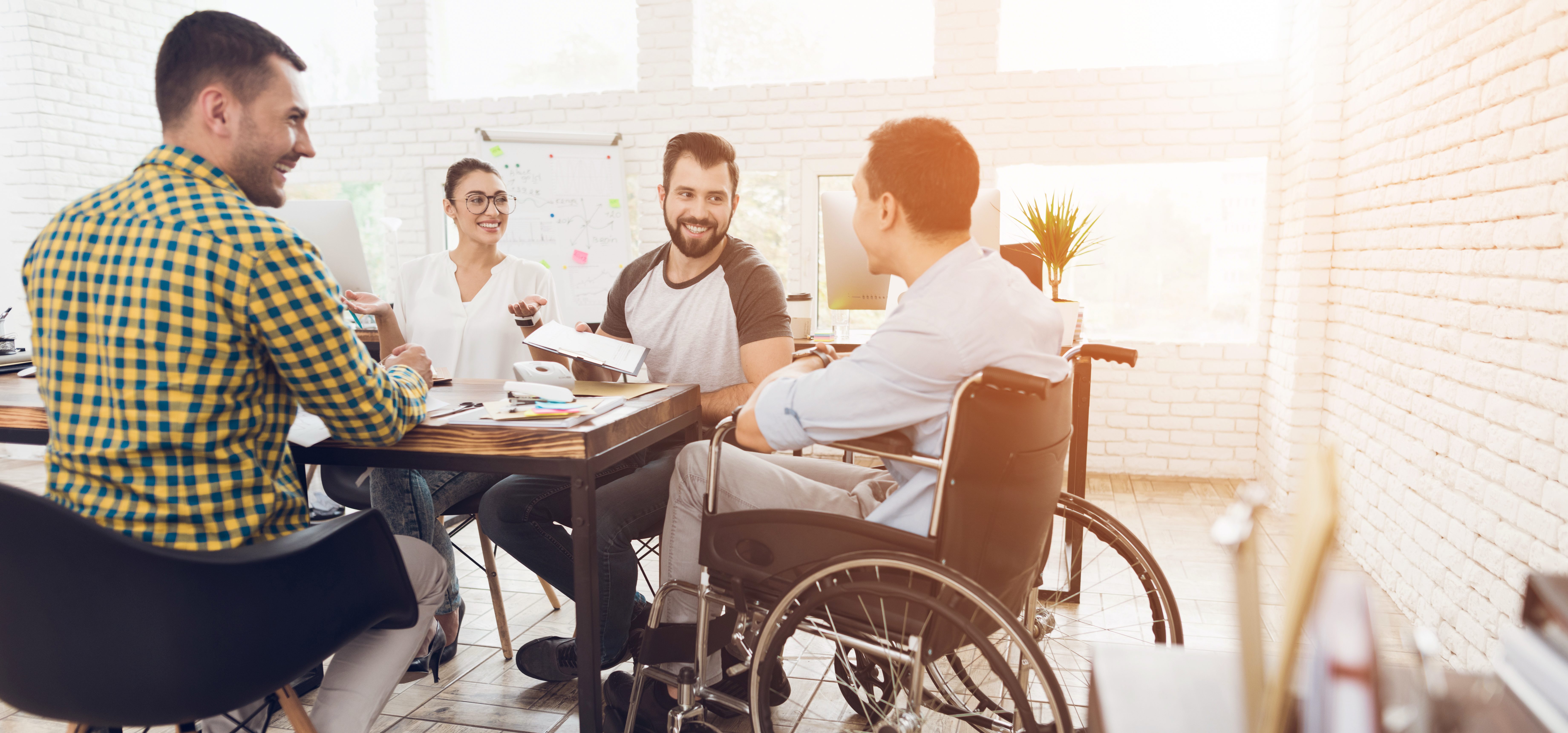 A man in a wheelchair communicates cheerfully with employees of the office during a business meeting.