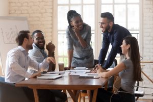 Cheerful mixed race young business partners enjoying break time during brainstorming meeting at office. Happy diverse colleagues laughing, having fun during discussing working issues in boardroom.