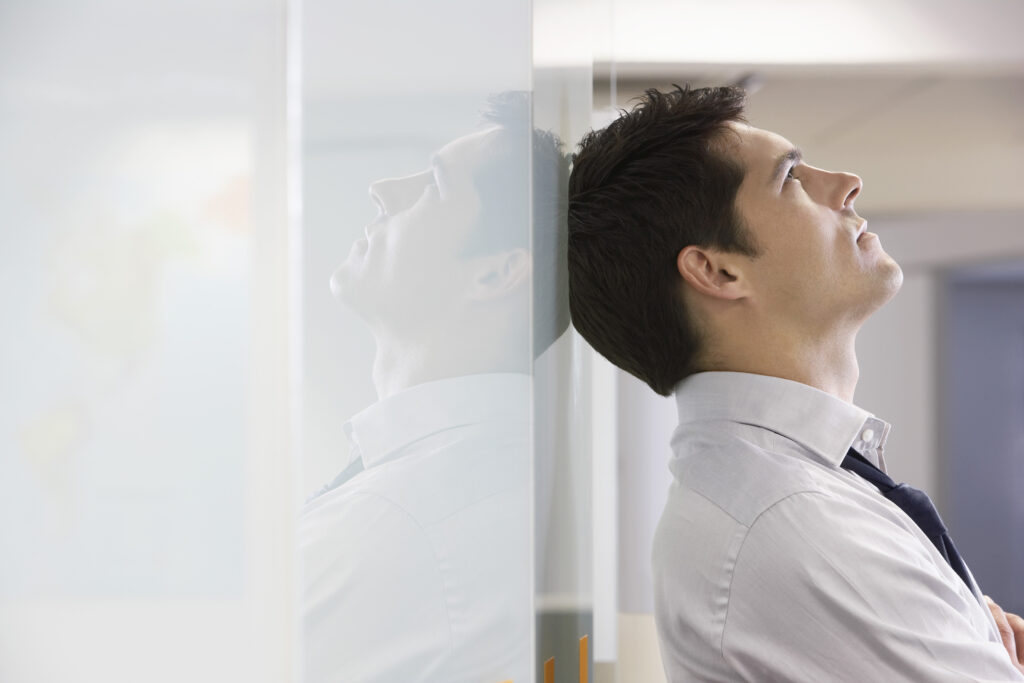 Unhappy businessman leaning back against office wall and looking at ceiling.