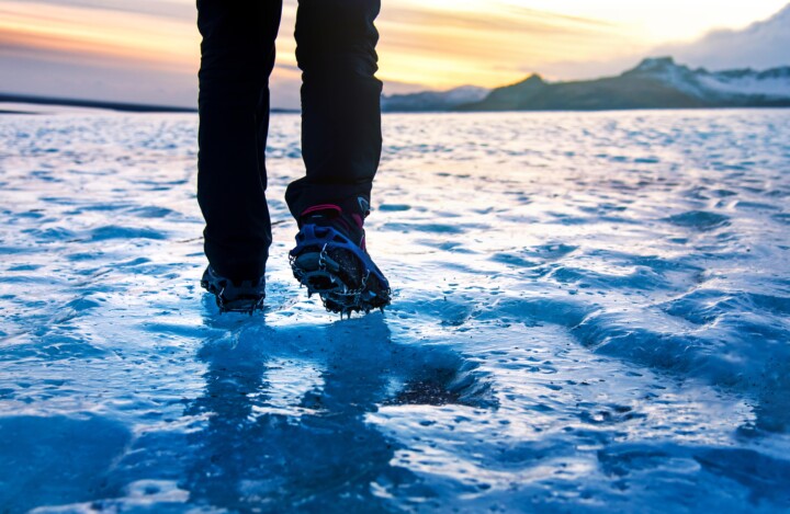 Person with spikes on boots walking on ice. Mountains in background.