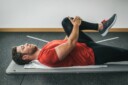 Man laying on yoga mat stretching lower back and leg.