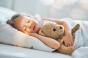 Young girl sleeping with a plush bear.