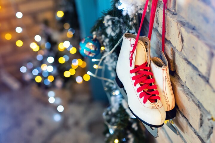 Pair of white vintage leather skates with red laces hanging on old rustic brick wall with blurred lights on christmas tree decoration. Cozy scenic christmas card interior winter holidays background.