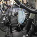 Face-mask hanging off handlebars of an exercise bike in a gym.