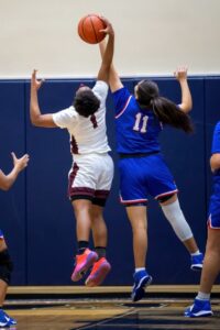 two female varsity basketball players reach for the basketball during a game