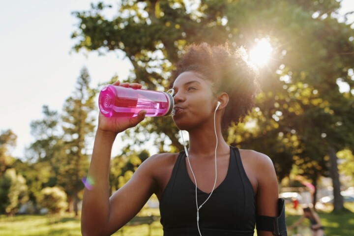 Young african american female fitness athlete listening to music and drinking water after exercising.
