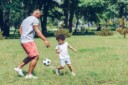Father and child playing soccer in the park.