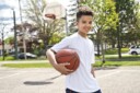Adolescent boy holding a basketball on the court with net in background.