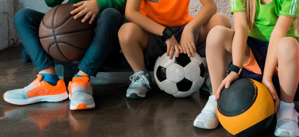 Cropped view of children sitting on step platforms with balls in gym, panoramic shot