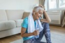 Older woman sitting, drinking water, and listening to music after working out.