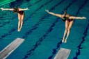 Two women synchronously jumping off diving boards.