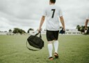 Man strolls on to a soccer pitch carrying a bag.