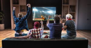 Groupe de supporters regardant un match de football sur le canapé de leur domicile. Ils célèbrent un but. 