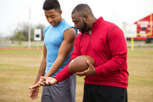 Older male athlete mentors younger male athlete in football technique