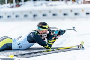 Side view of a male biathlon athlete shooting during a competition in winter.