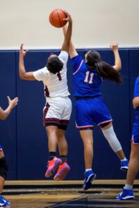 Two young female basketball athletes jump for the ball during a game.