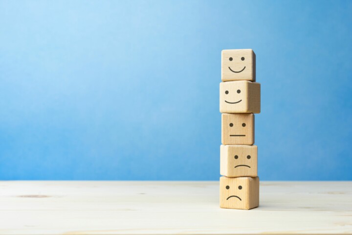 Wooden blocks stacked on a table, each has a different smiling face (happy to unhappy).