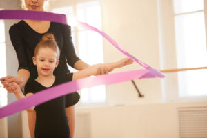 Little girl doing gymnastics moves with ribbon in studio lit by warm sunlight