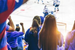 Rear view of female hockey spectators watching a hockey game in an arena.