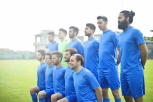 Side-view of a men's soccer team lined up in two rows before the start of a match. Wearing blue uniforms.