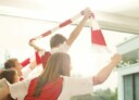 Family in red and white sports jerseys cheering in living room