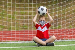 School kid with mask and soccer ball in a physical education lesson.