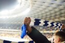 Sports fan in a stadium holding up a blue-and-white scarf to support his favourite team.