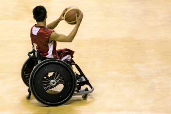 Wheel chair basketball player holding a ball and rolling across a hardwood gym floor.