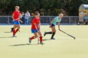 A girl in a red shirt playing field hockey on a sunny day. A player in a blue shirt is playing on defence.