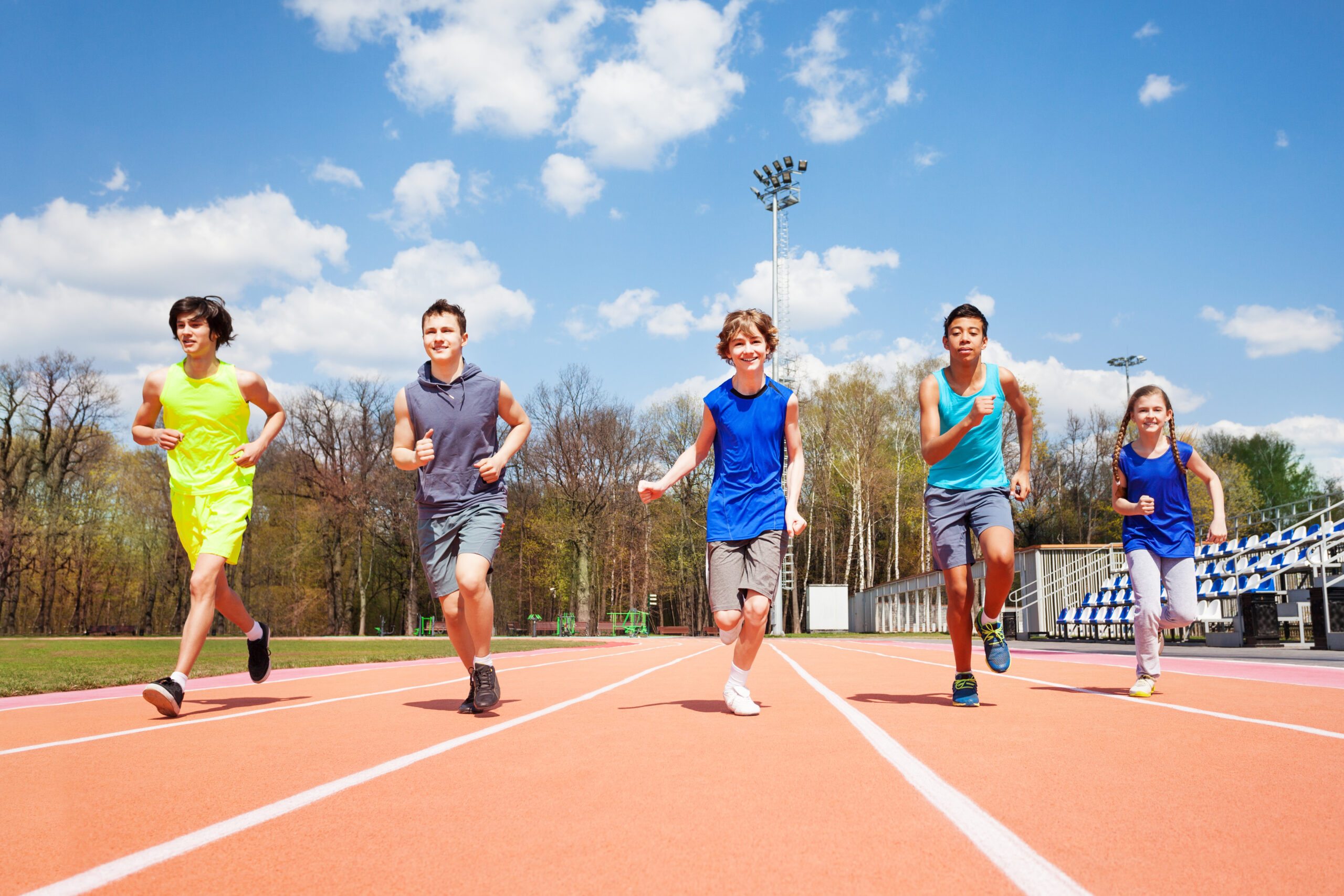 Portrait of five teenage sprinters, running together on the racetrack in spring