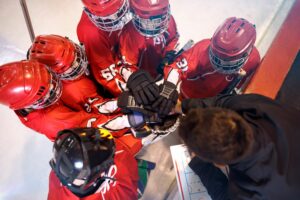 Youth hockey team putting hands together with coach in a huddle, showing teamwork