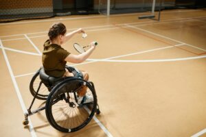 High angle portrait of young woman in wheelchair playing badminton during sports practice at indoor court.