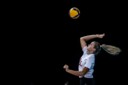 Side view of a female Volleyball Canada athlete jumping into the air to serve the ball, action shot against a black background.