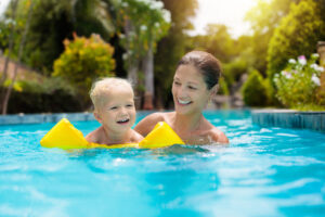 Mother and baby in outdoor swimming pool of tropical resort. Kid learning to swim. Mom and child playing in water. Family summer vacation in exotic destination. Active and healthy sport for kids.