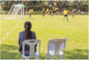 Une fille assise aux abords du terrain qui regarde les autres jouer au soccer