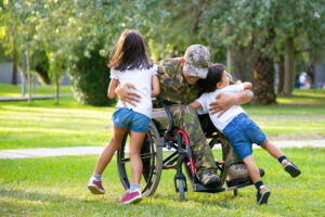 Happy disabled military man in wheelchair returning home and hugging kids. 