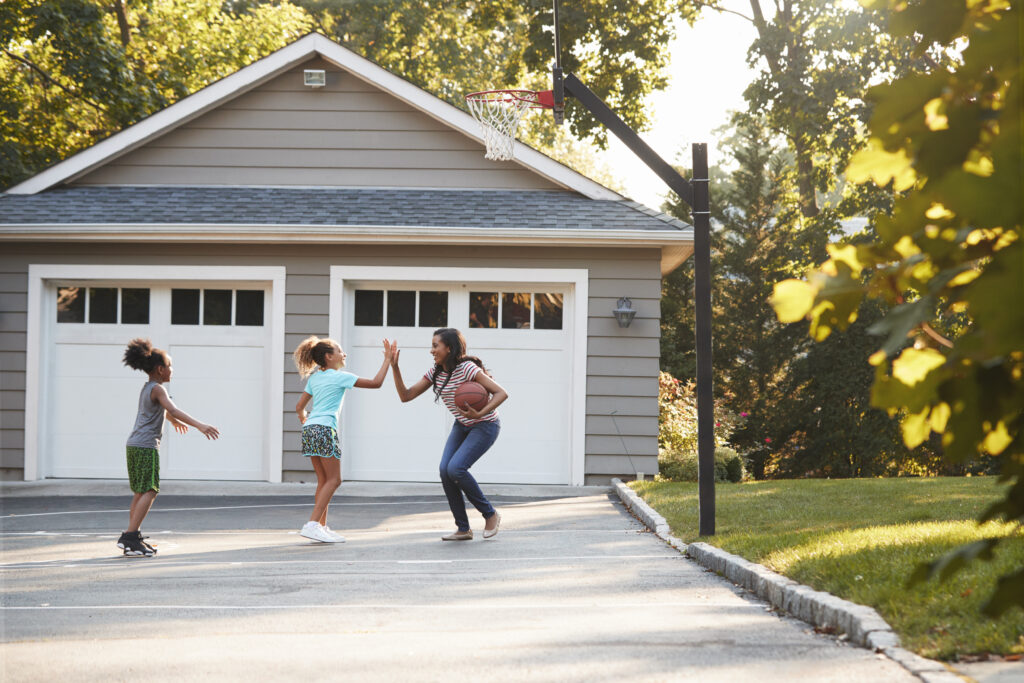 Mother And Children Playing Basketball On Driveway At Home