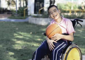 Un enfant handicapé en fauteuil roulant joue au basket-ball sur la pelouse devant la maison comme les autres personnes, Style de vie d'un enfant spécial, Vie à l'âge de l'éducation des enfants, Concept d'enfant handicapé heureux.