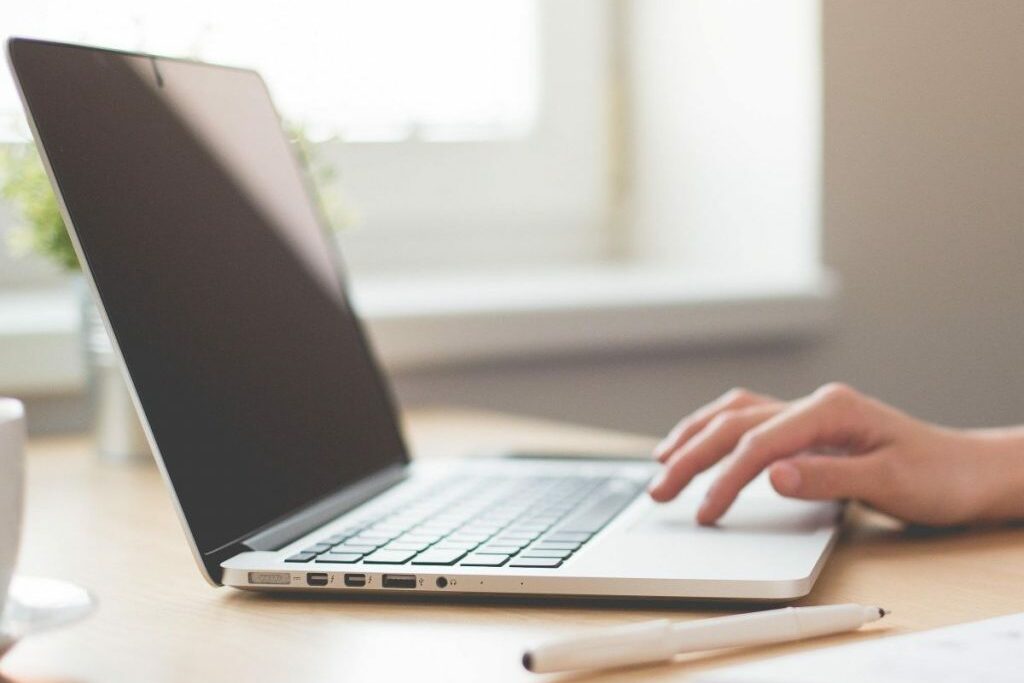 Laptop sitting on a desk with a hand typing