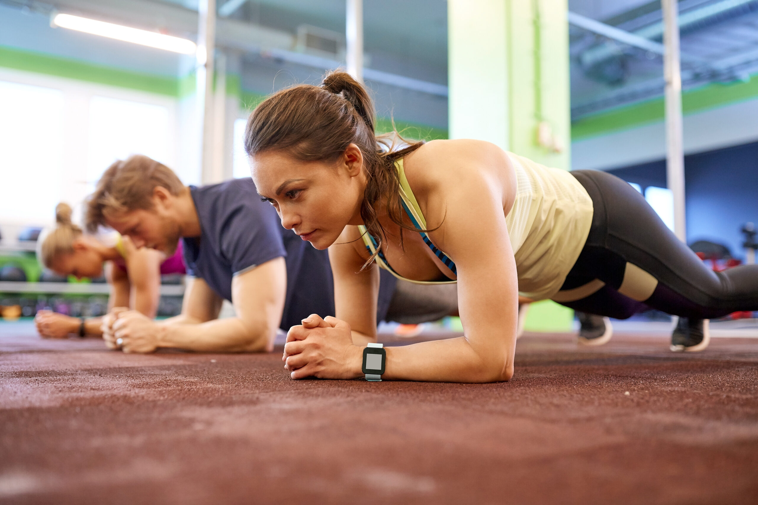 Fitness, sport, exercising and people concept - woman with heart-rate tracker at group training doing plank exercise in gym