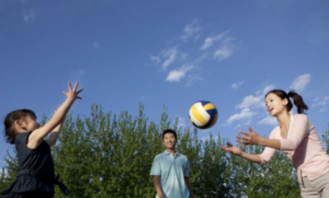 Mother, father and daughter playing volleyball in the park. 