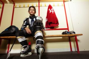 Youth hockey player sitting on a locker room bench with his equipment on.