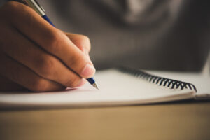 A man's hand with pen writing on notebook.