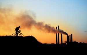 A cyclist rides near industrial smokestacks