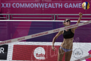 Beach volleyball player reaching for ball over the net with Commonwealth Games logo in the background.