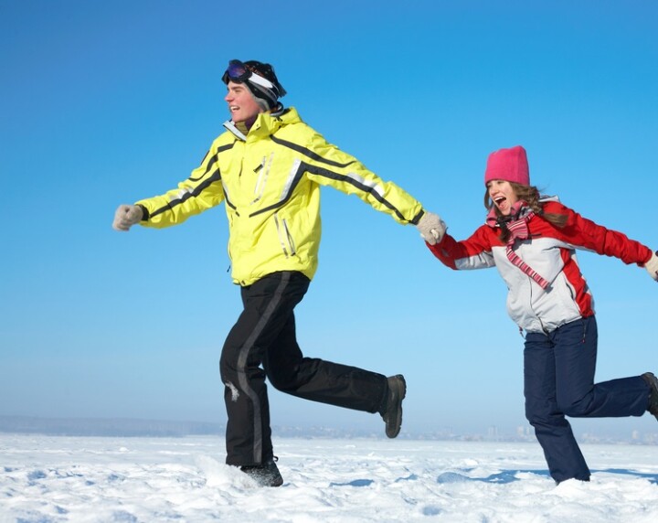 3 people dressed in winter clothing are holding hands and running through the snow.